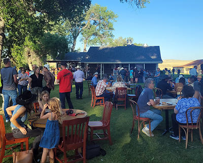 Guests standing and sitting at tables mingle in the grove at the TA Ranch.